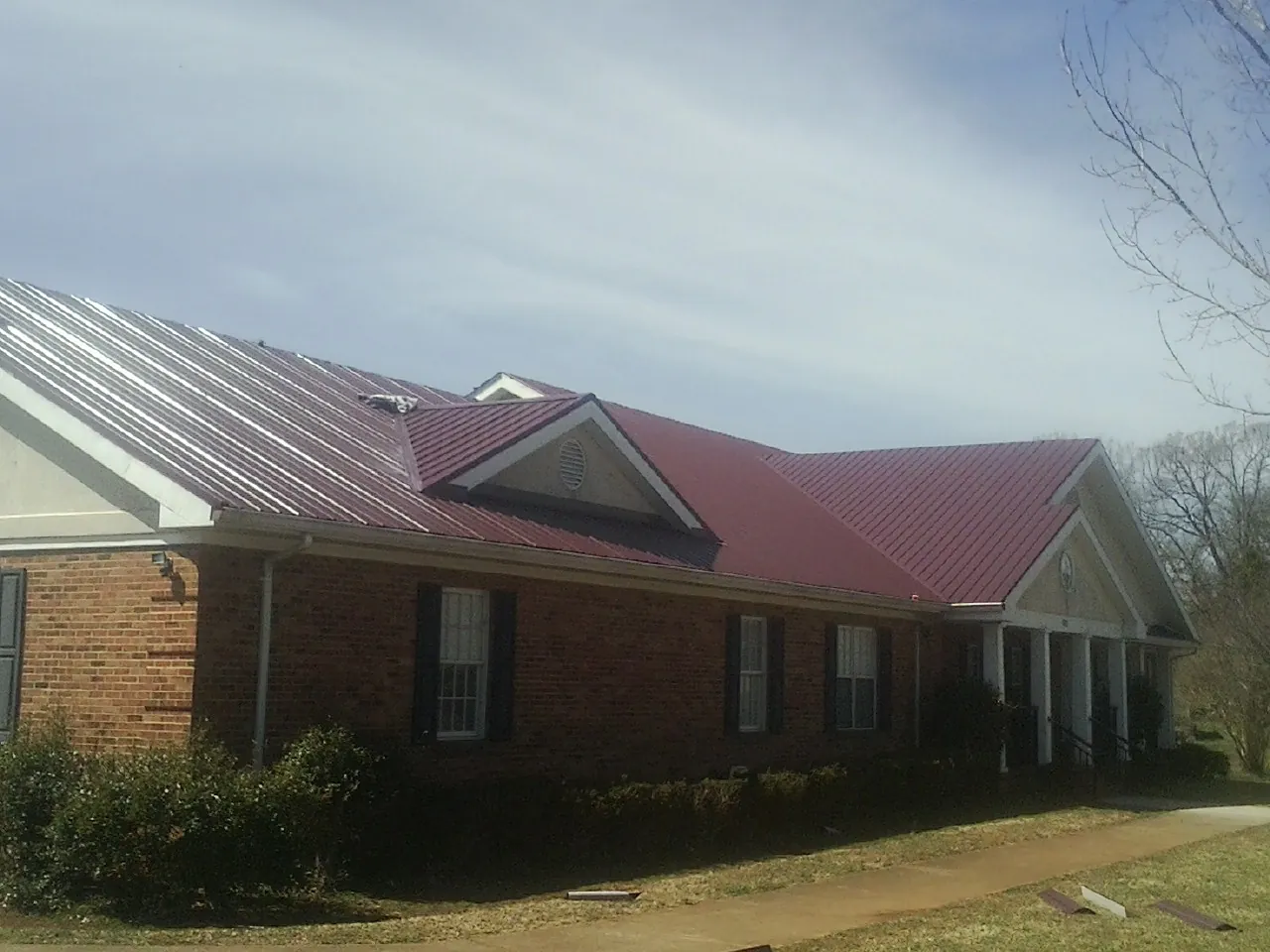 Red metal roof with gabled entries on a long brick building, from a Hail Damage Roof Repair job in Windsor Mill