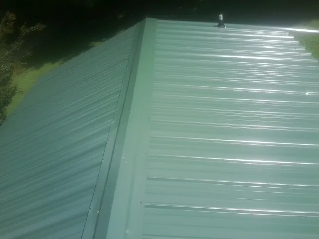 New green metal panels meeting at the ridge of a roof — Flat Roof Repair work by our crew in Windsor Mill