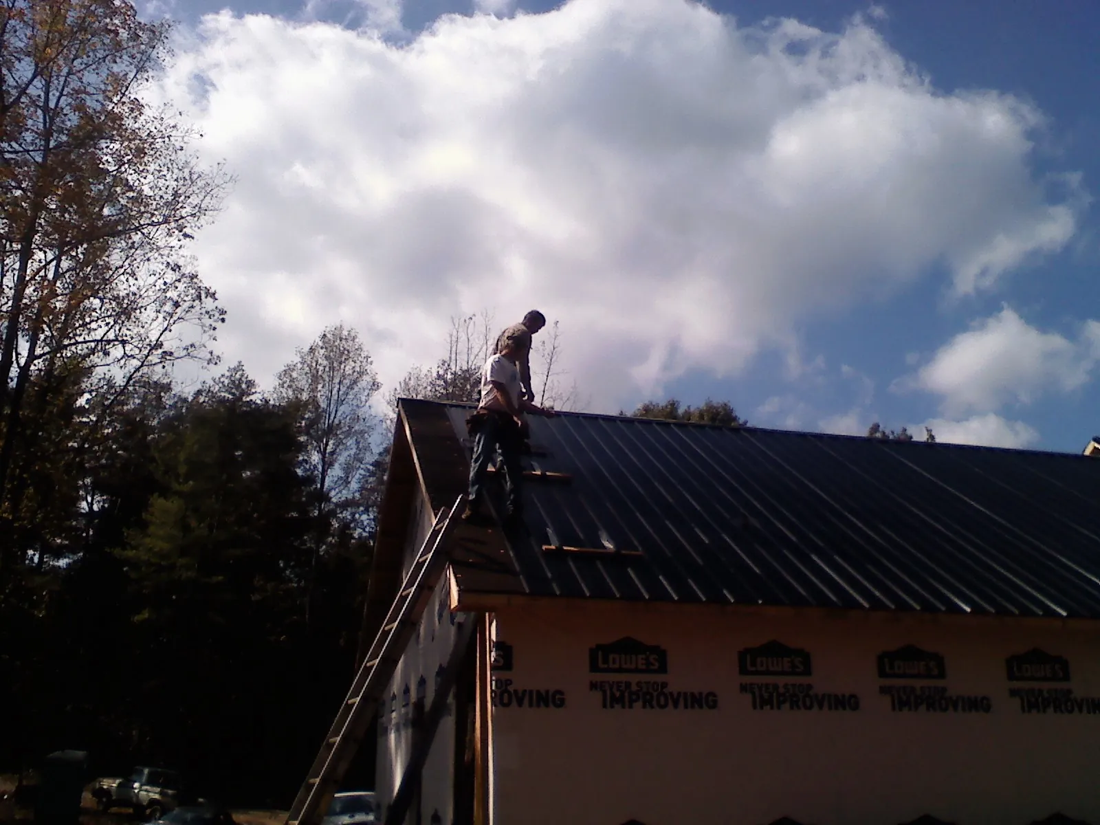Roofer fastening dark metal panels high against a cloudy sky, from a Roof Inspection job in Windsor Mill