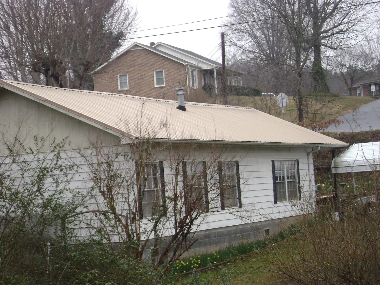 Tan metal roof on a white sided house set into a hillside — Commercial Roofing by Roofing Brothers in Windsor Mill